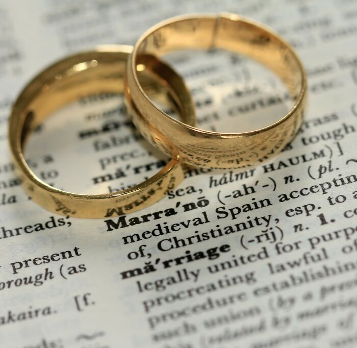 Two gold wedding rings placed on a dictionary page showing the word marriage symbolizing a new bride's side piece exposure. Two gold wedding rings placed on a dictionary page showing the word marriage symbolizing a new bride's side piece exposure.