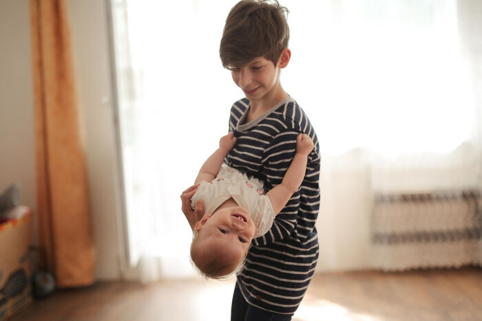 Young babysitter holding a baby upside down in a warmly lit room, capturing a playful moment during childcare.