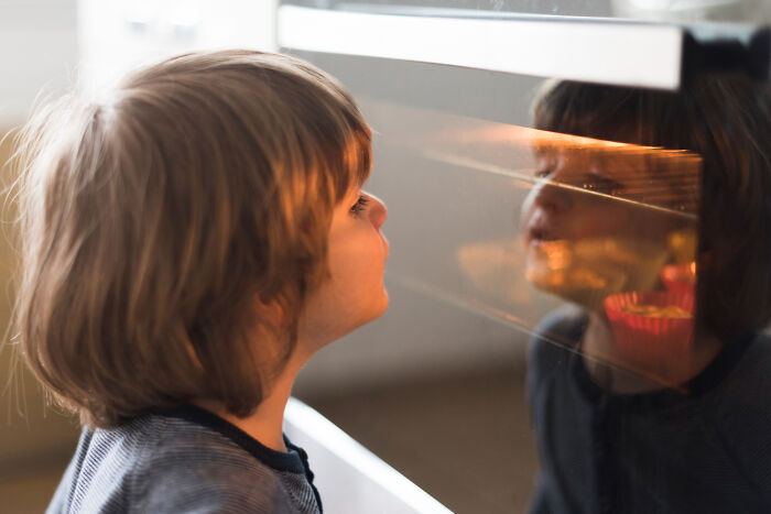 Child looking into an oven window with a reflection, illustrating babysitters' bedtime stories and horror experiences.
