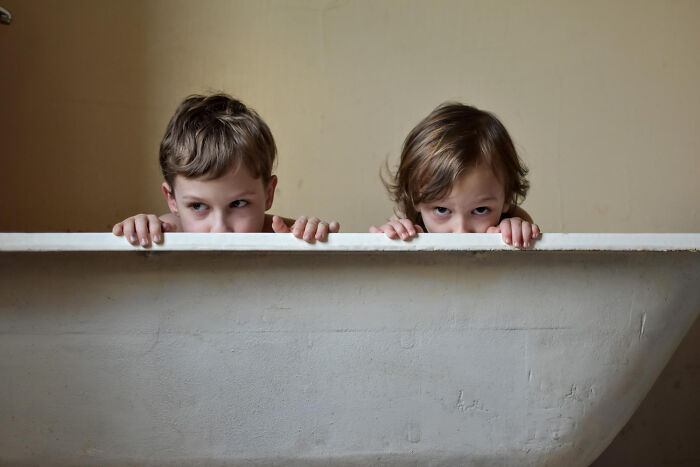 Two young children peeking over the edge of a bathtub, illustrating babysitters' horror experiences with bedtime stories.