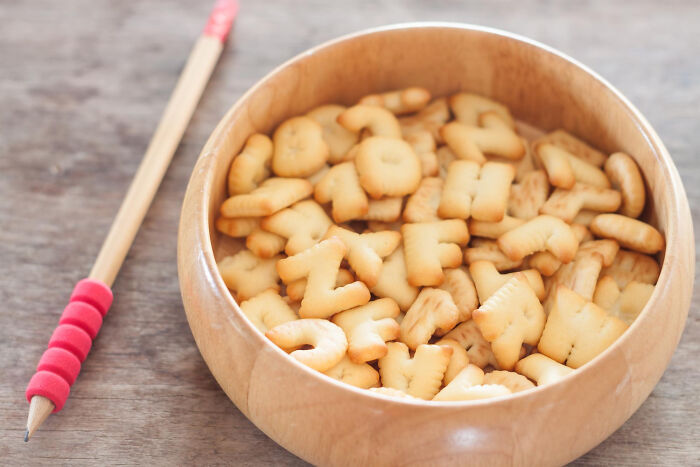 Wooden bowl filled with alphabet cookies next to a pencil, representing babysitters sharing horror bedtime stories.
