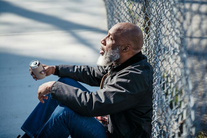 Man with gray beard sitting by a fence holding a can, reflecting themes of babysitters living horror experiences.