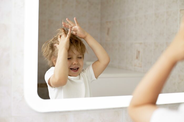 Young child playing and making faces in a bathroom mirror, relating to babysitters and bedtime stories horror experiences.
