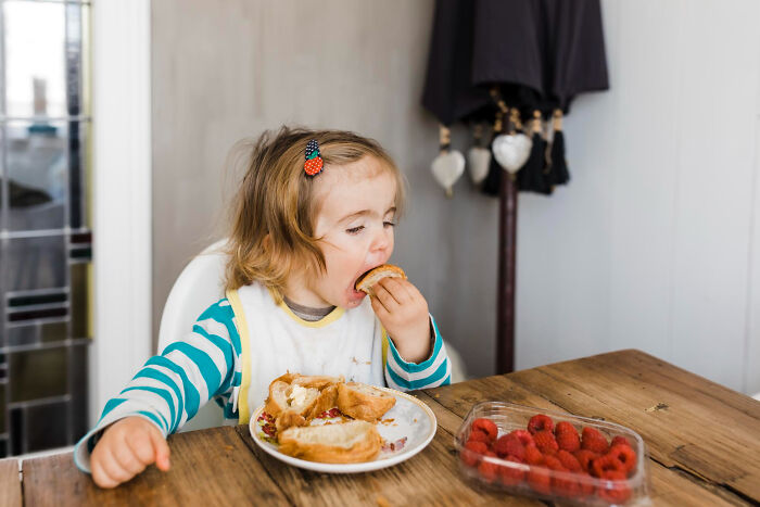 Young child eating sandwich at a wooden table, illustrating everyday moments babysitters experience during bedtime stories.
