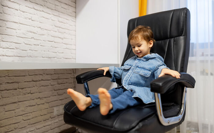 Young child sitting barefoot on an office chair indoors, illustrating babysitters experiencing unexpected horror during bedtime stories.