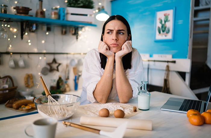 Woman baking cupcakes for son’s birthday, looking frustrated in a kitchen with baking ingredients and laptop nearby. Woman baking cupcakes for son’s birthday, looking frustrated in a kitchen with baking ingredients and laptop nearby.