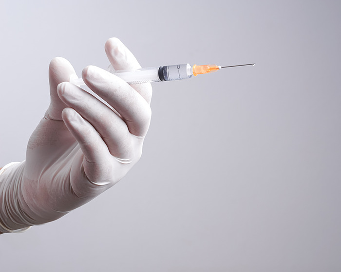 Hand in white glove holding a syringe with needle, representing Scrotox cosmetic trend and medical warnings for men. Hand in white glove holding a syringe with needle, representing Scrotox cosmetic trend and medical warnings for men.