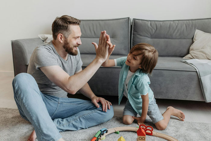 Man giving high five to young boy playing with toys on carpet, illustrating lazy entitled disabled bro situation. Man giving high five to young boy playing with toys on carpet, illustrating lazy entitled disabled bro situation.