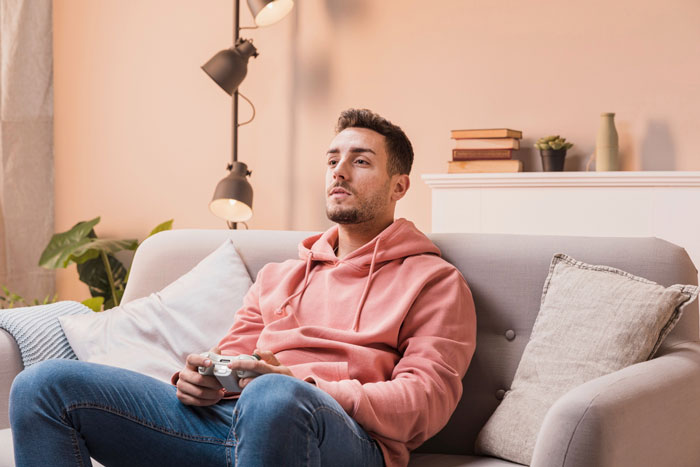 Young man in a casual pink hoodie playing video games, showing signs of laziness and entitlement at home. Young man in a casual pink hoodie playing video games, showing signs of laziness and entitlement at home.