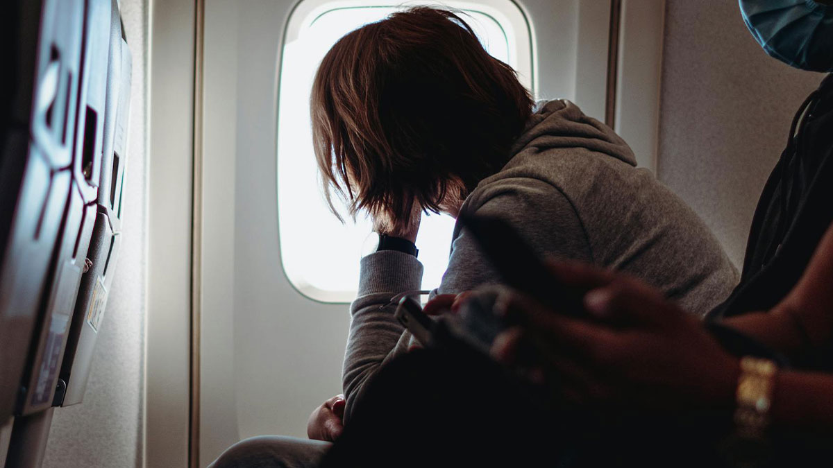 Passenger on Korean Airlines looking distressed by airplane window during a medical crisis while crew nearby use phones.
