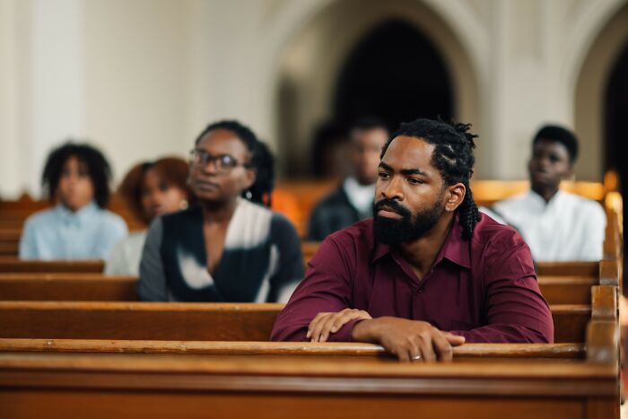 Man with a beard sitting in a pew looking thoughtful, surrounded by others, illustrating out of touch moments.