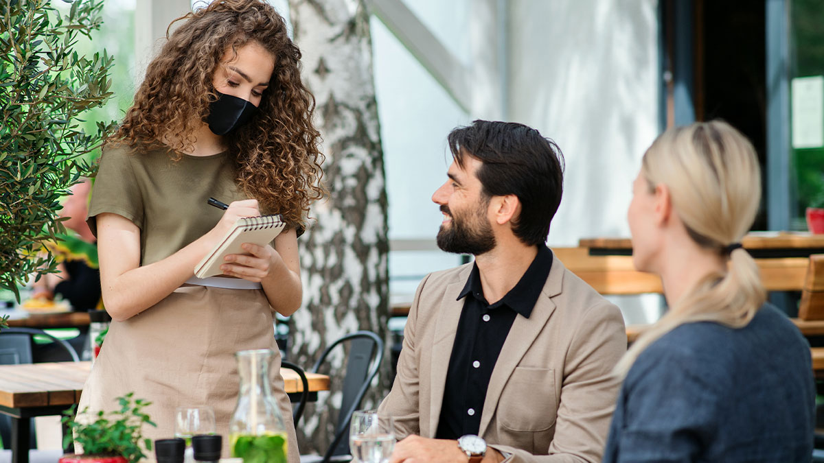 Waitress wearing mask taking order from customers at outdoor restaurant, illustrating weird waitress and tap water request.