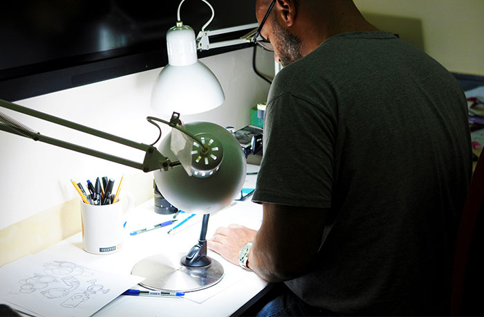 Man at desk with lamp and sketches, representing school gossip facts exposed in a focused workspace setting.