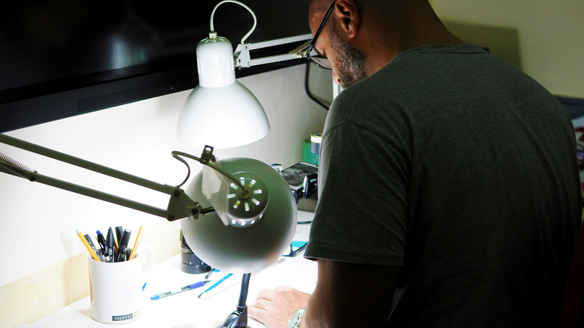 Man wearing glasses working at a desk with lamps and pens, symbolizing school gossip facts revealed openly.
