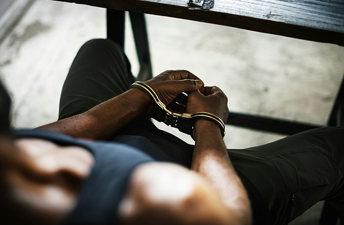 Person in handcuffs sitting at a table with hands clasped, illustrating school gossip turning into straight facts exposed.