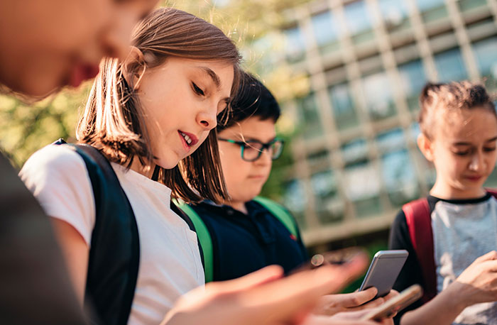 Group of school students outdoors, focused on their phones, representing school gossip and facts exposed.