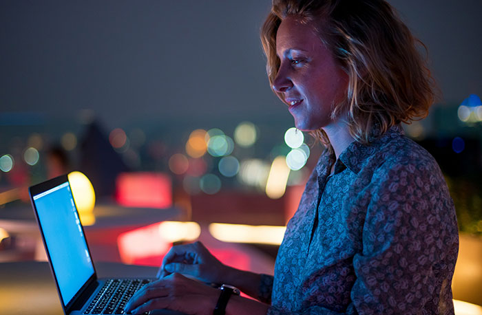 Young woman using laptop at night with city lights in the background, illustrating school gossip facts exposed online.