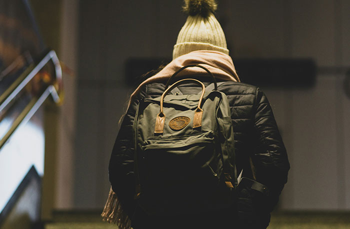 Student wearing a beanie and backpack walking up stairs, representing school gossip and facts exposed openly.