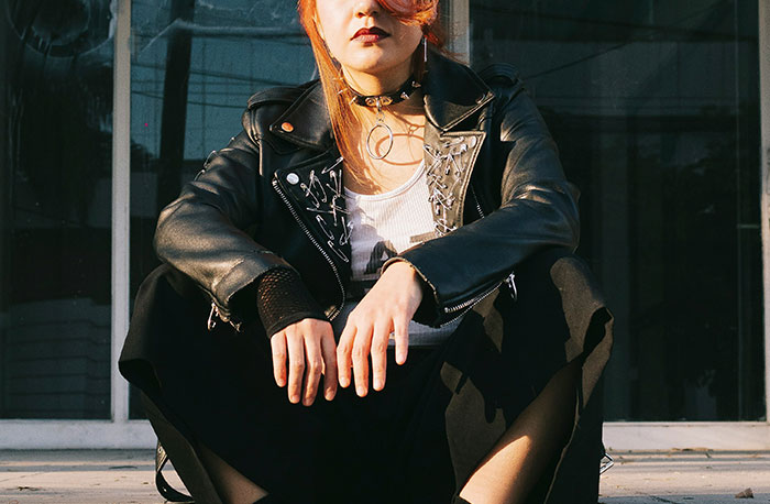 Young person in black leather jacket and choker, seated outdoors, reflecting school gossip revealed as straight facts.