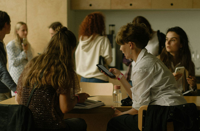 Group of young people in casual clothes sharing school gossip and facts using smartphones in an indoor setting