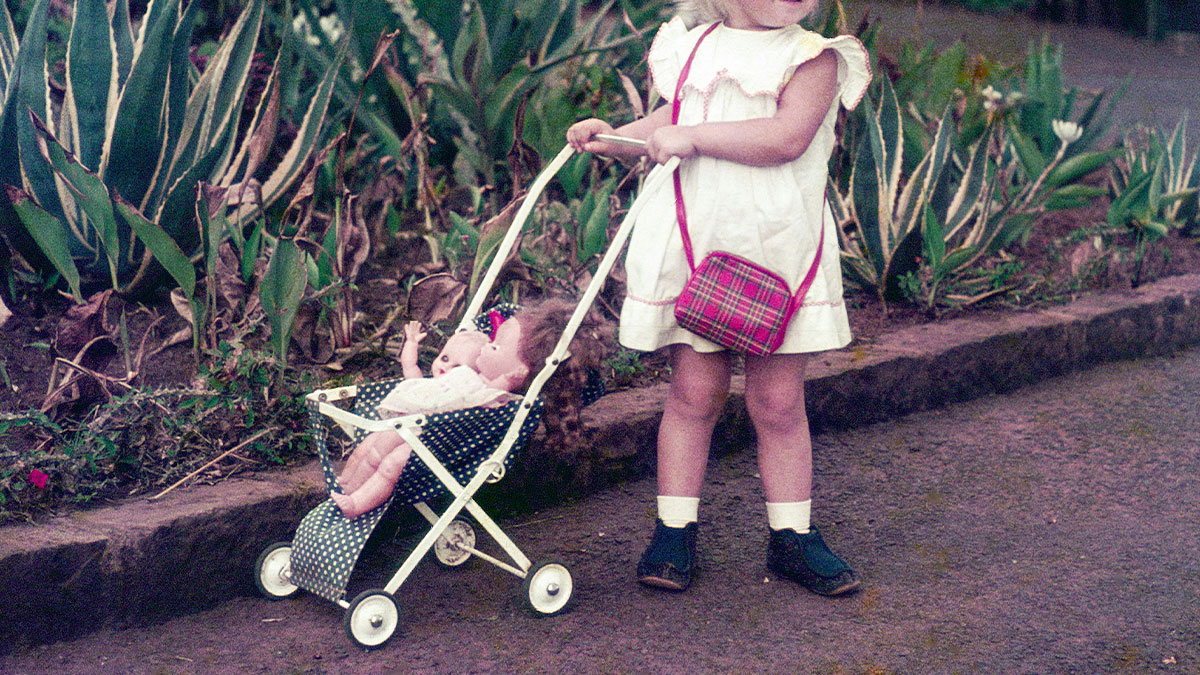 Young child pushing doll stroller outdoors, vintage photo reflecting dark secrets people found about family members.