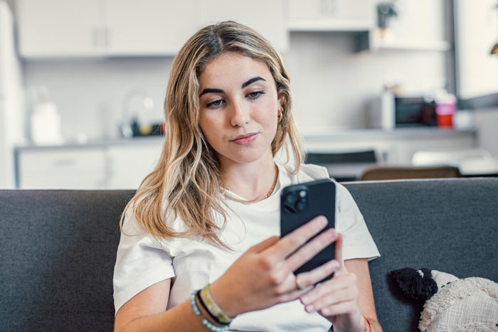 Young woman sitting on a couch looking at her phone with concern, capturing sister boyfriend relationship drama emotions. Young woman sitting on a couch looking at her phone with concern, capturing sister boyfriend relationship drama emotions.