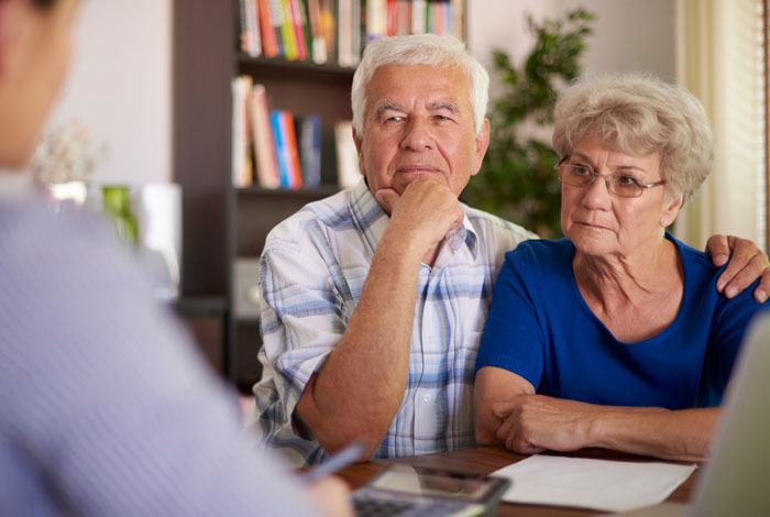 Elderly couple in serious discussion during a meeting, reflecting on challenges of babysitting autistic sibling. Elderly couple in serious discussion during a meeting, reflecting on challenges of babysitting autistic sibling.