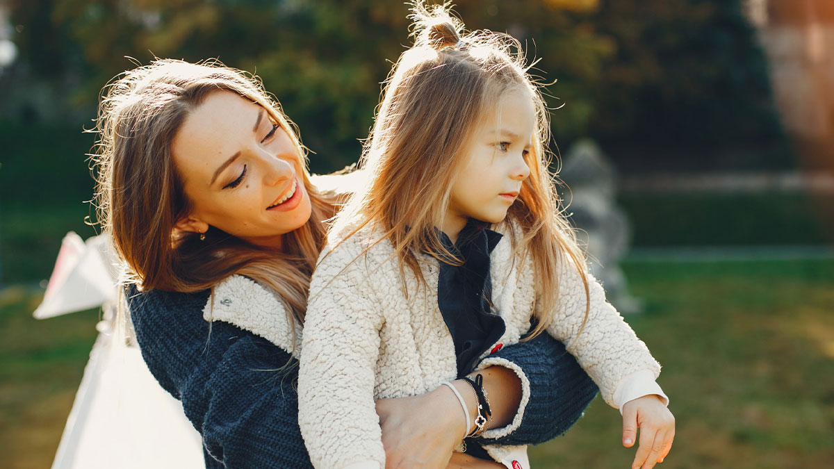40-year-old aunt smiling and holding young girl outdoors, refusing to be a free sitter for family couple.