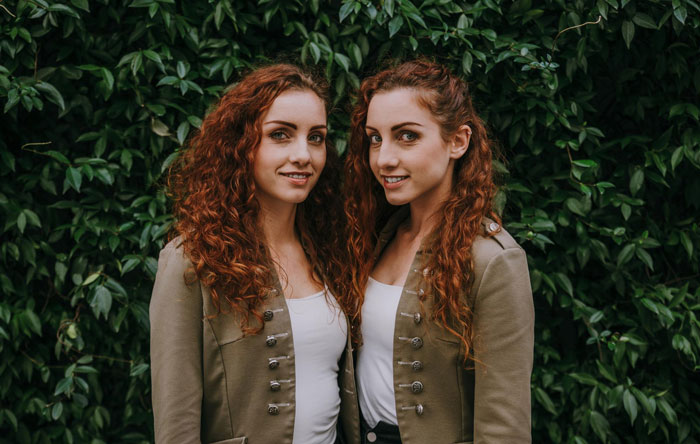 Two red-haired twin sisters standing close together outdoors, illustrating bride tries to erase twin at wedding. Two red-haired twin sisters standing close together outdoors, illustrating bride tries to erase twin at wedding.