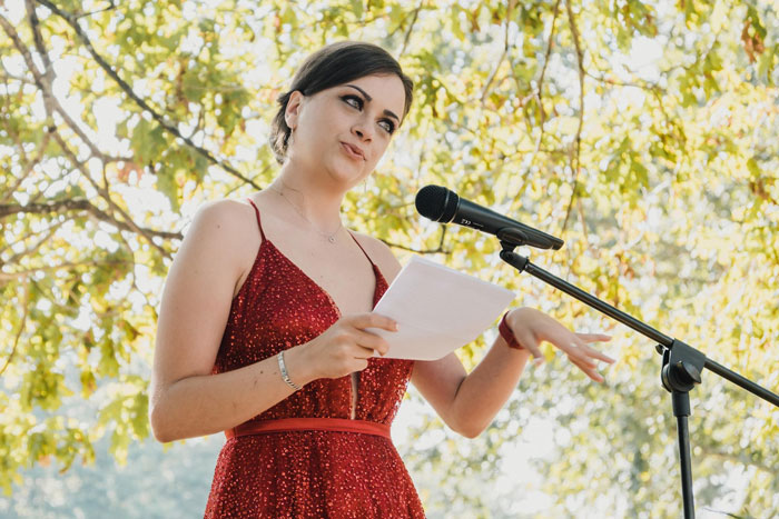 Bride in a red dress giving a speech at an outdoor wedding, highlighting family favoritism and twin rivalry. Bride in a red dress giving a speech at an outdoor wedding, highlighting family favoritism and twin rivalry.