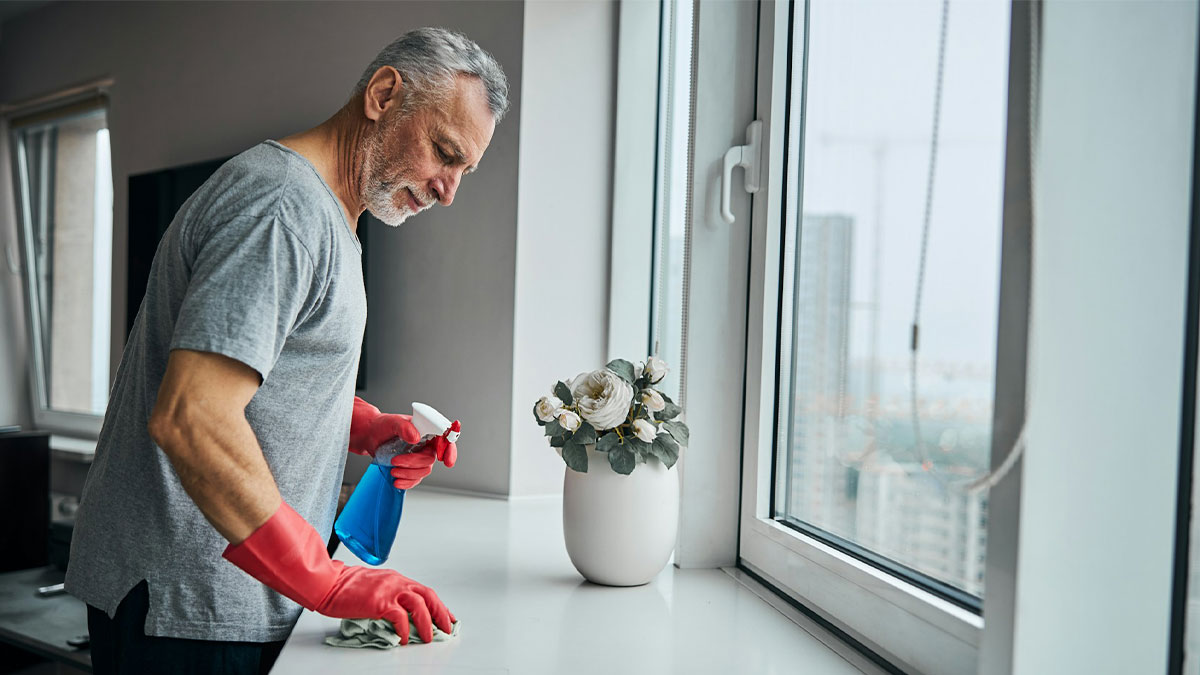Older man in red gloves cleaning a window sill, illustrating tips from men in happy marriages for great relationships.