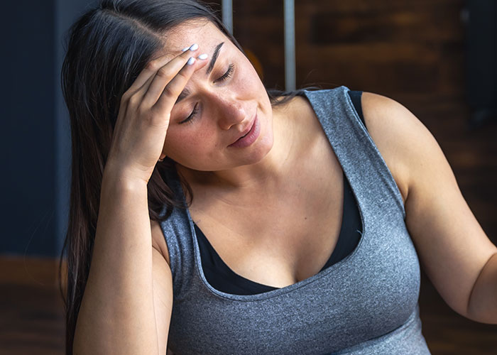 Woman in a gray tank top looking thoughtful and stressed, reflecting on her body and personal transformation journey. Woman in a gray tank top looking thoughtful and stressed, reflecting on her body and personal transformation journey.
