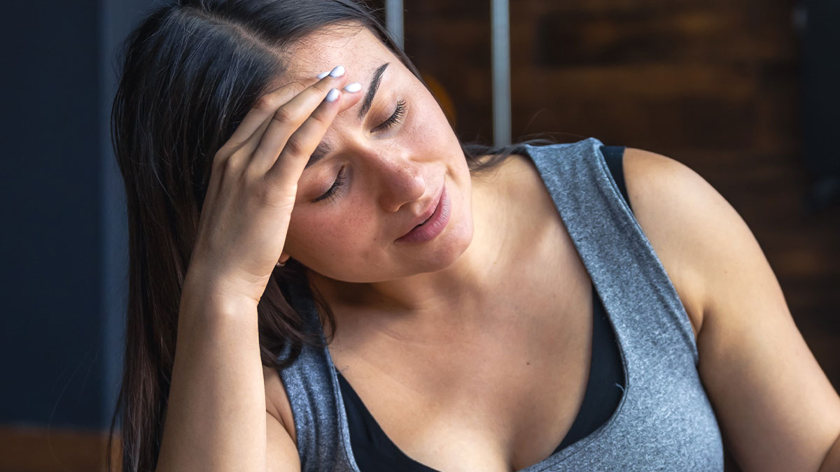 Woman in gray tank top looking thoughtful and concerned, reflecting on her body and emotions at home.