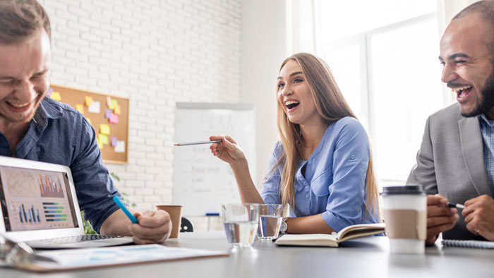 Three coworkers laughing and discussing at a meeting, illustrating workplace harassment and office conflict issues. Three coworkers laughing and discussing at a meeting, illustrating workplace harassment and office conflict issues.
