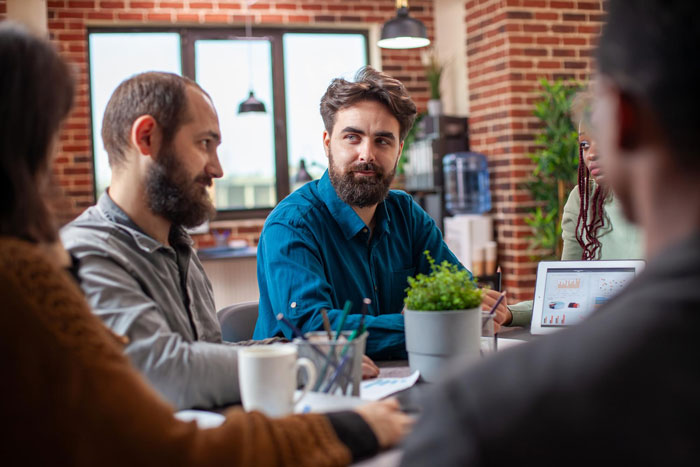 A group of coworkers in a modern office discussing workplace harassment concerns during a team meeting.