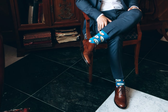 Man in navy suit and brown shoes sitting with colorful socks visible, illustrating workplace harassment concept. Man in navy suit and brown shoes sitting with colorful socks visible, illustrating workplace harassment concept.