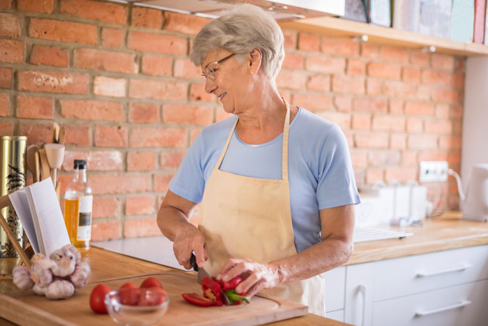 Elderly woman preparing food in kitchen, highlighting parents' food causing daughter to feel sick and worried.