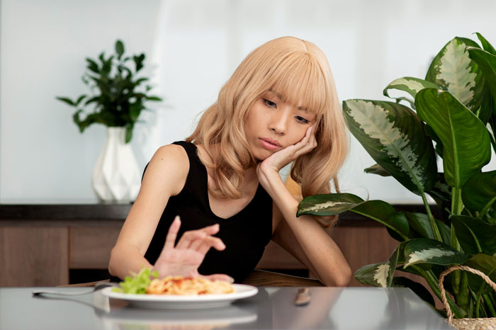 Young woman looking sick and worried while refusing to eat parents' food, worried about being poisoned or getting ill.