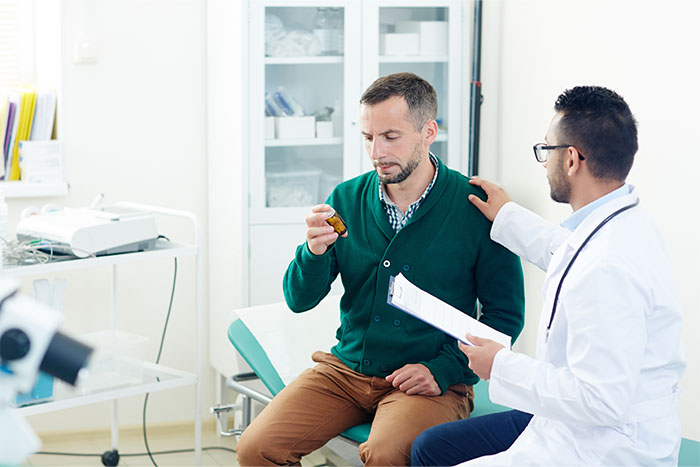 Man sitting in a clinic looking at a pill bottle while a doctor comforts him, illustrating ways people found out partner was cheating.