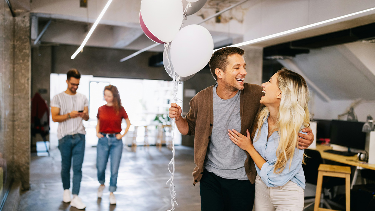 Couple laughing and holding balloons in a casual office setting, illustrating crazy and unhinged ways people found out cheating.