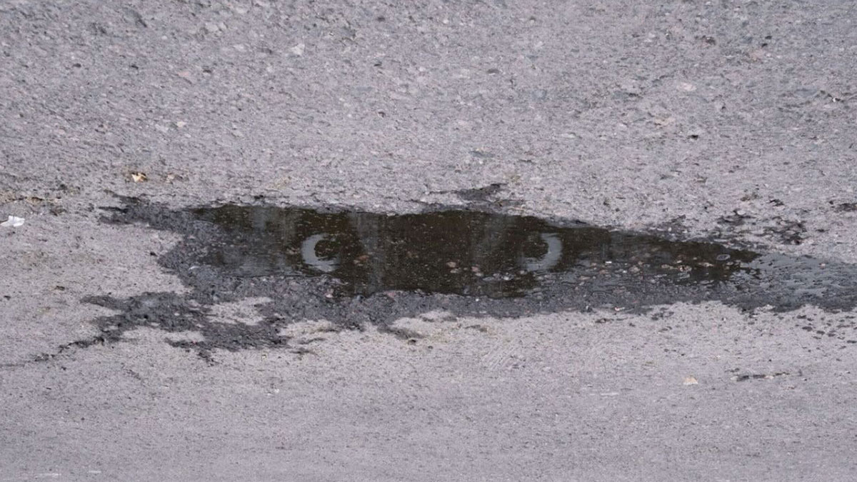 Reflection in a street puddle resembling a face with eyes, showcasing entertaining street photograph timing.