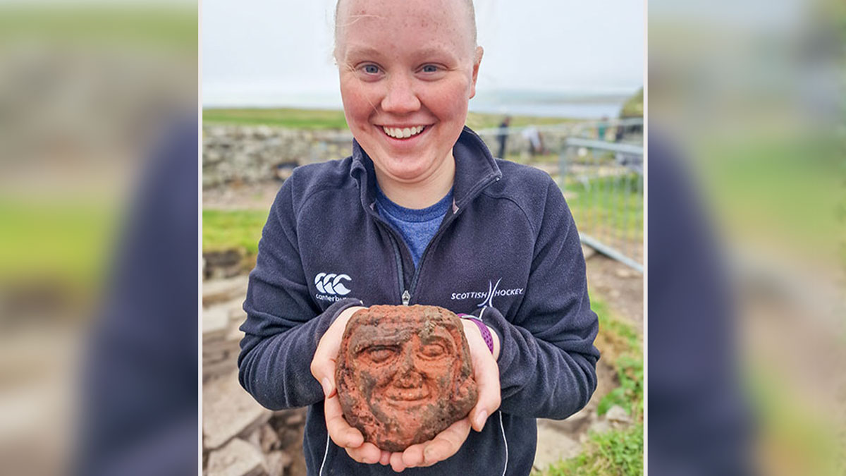 Archaeology student holding creepy ancient head carving discovered on a farm with striking facial features that appear to stare back.