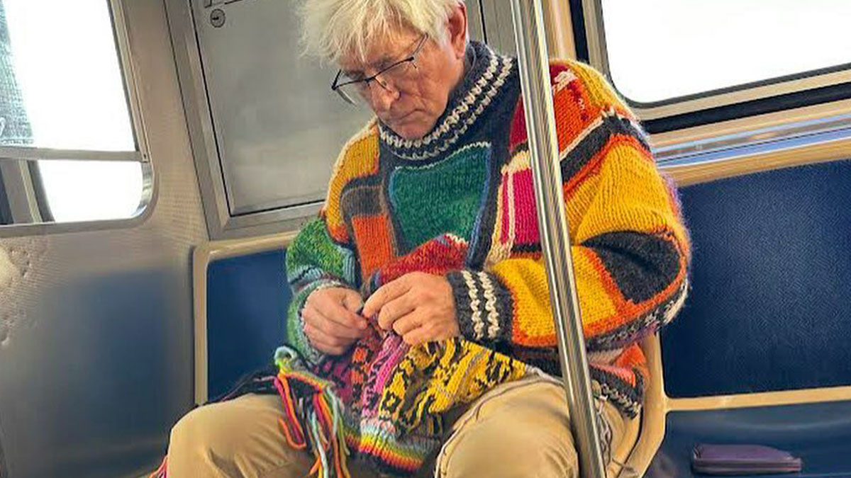 Elderly man in a colorful, stylish sweater knitting on a subway, showcasing cool and stylish grandparents fashion.