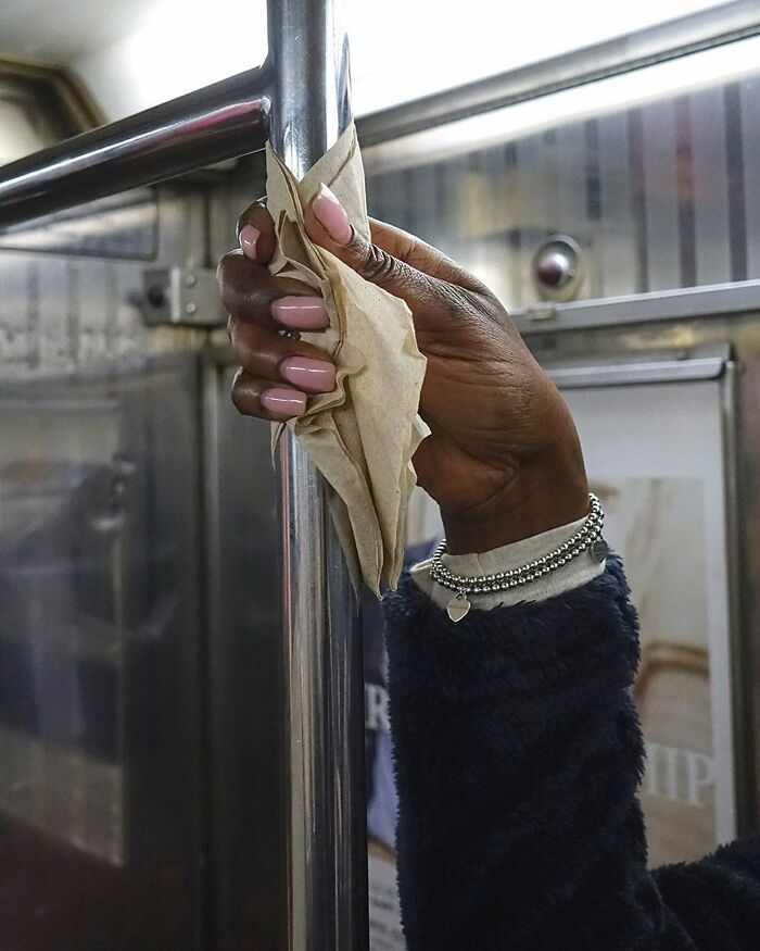 Hand holding subway pole in New York with crumpled paper, showcasing people carrying cute and weird things in their hands.