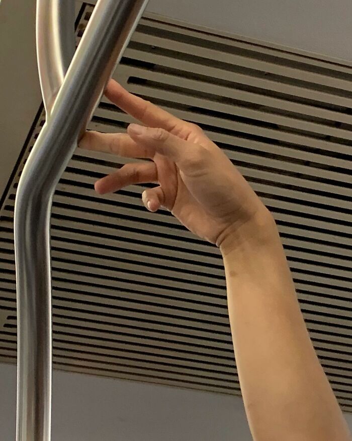 Hand holding onto a subway pole, illustrating people taking the subway in New York with unique items in their hands.