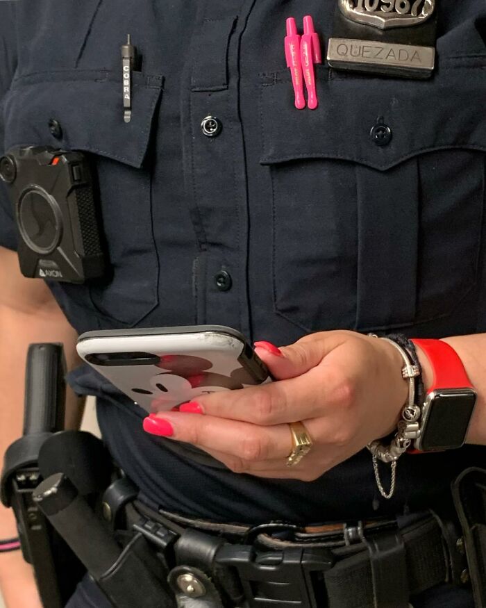 Police officer in New York subway holding a smartphone with a Mickey Mouse case and wearing a red smartwatch and pink nails.