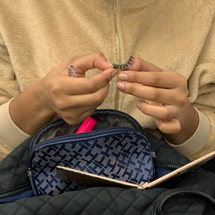 Person on New York subway holding false eyelashes above a patterned bag with a pink item inside.