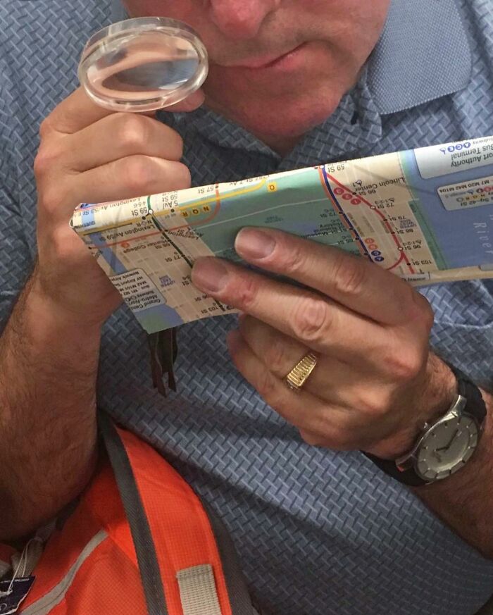 Man on New York subway holding a map purse and a magnifying glass while examining details closely.