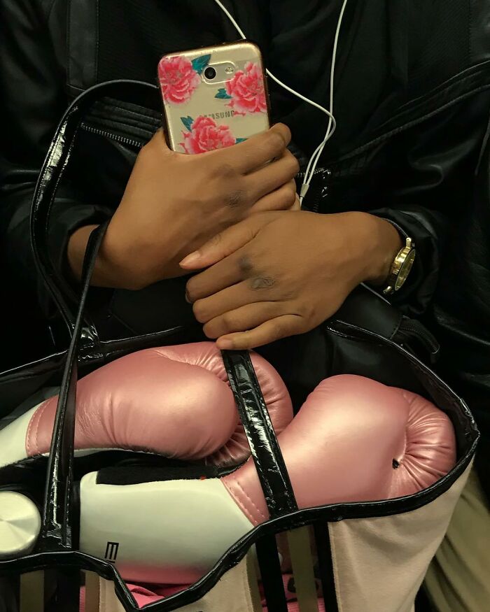 Person on New York subway holding phone with floral case and carrying pink boxing gloves in a bag.