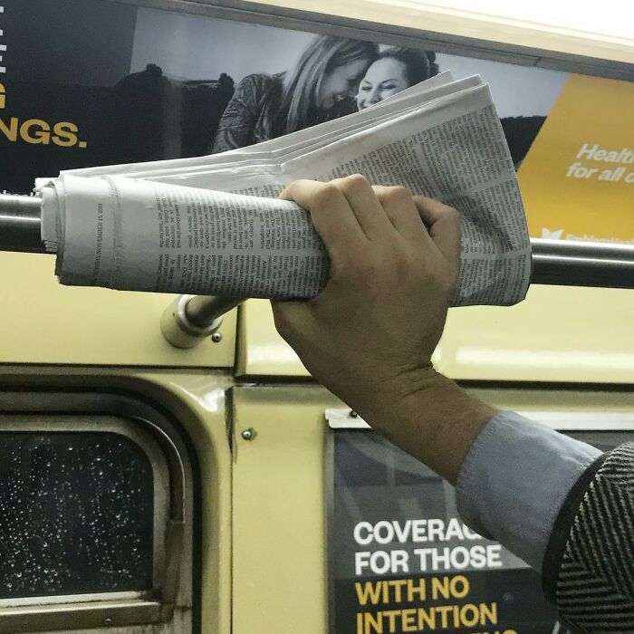 Person holding a rolled newspaper in hand while standing inside the New York subway with ads in the background.
